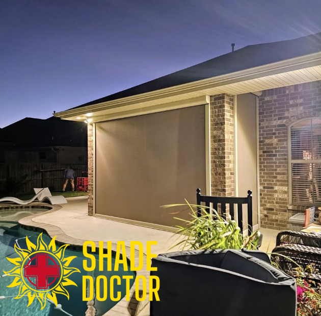 Patio with large tan retractable shade installed on a brick house at dusk, Shade Doctor logo visible