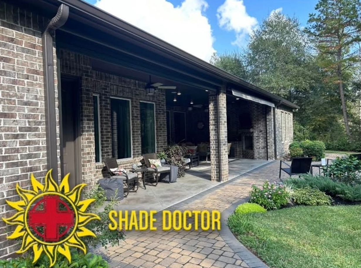 Brick house patio with covered porch, stone walkway, and lawn under blue sky; Shade Doctor logo at bottom left