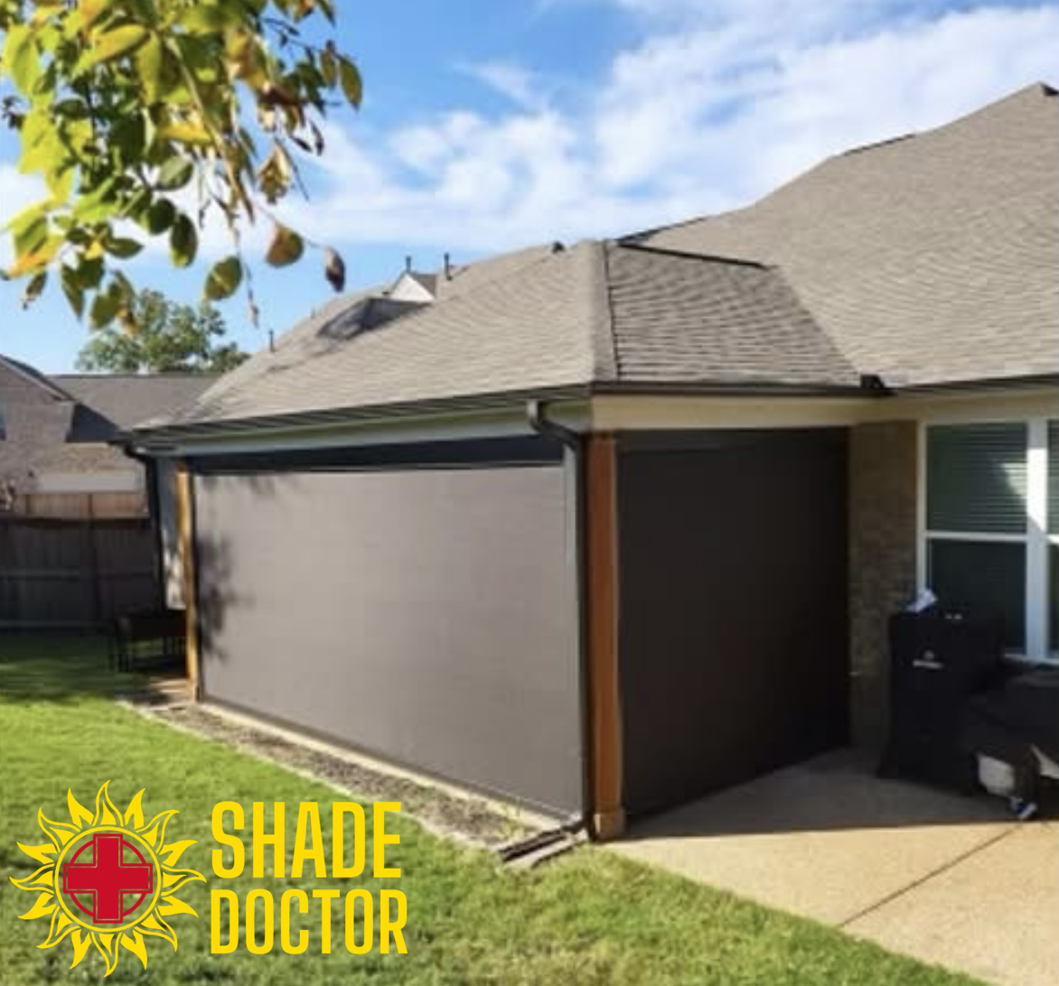 Patio with a gray retractable screen shade lowered beside a house in a backyard.