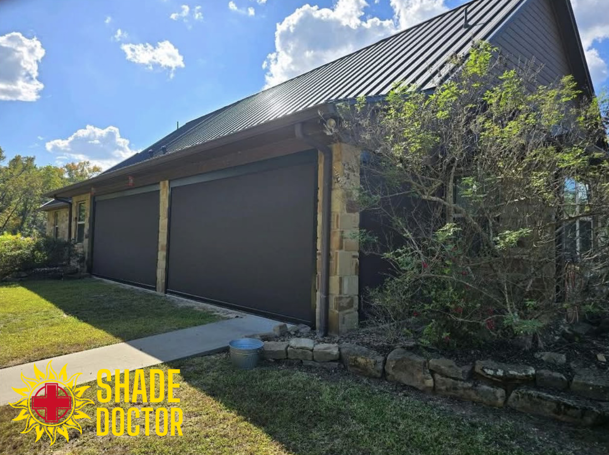 Garage with dark tinted roller doors, black metal roof, and a tree in front on a sunny day