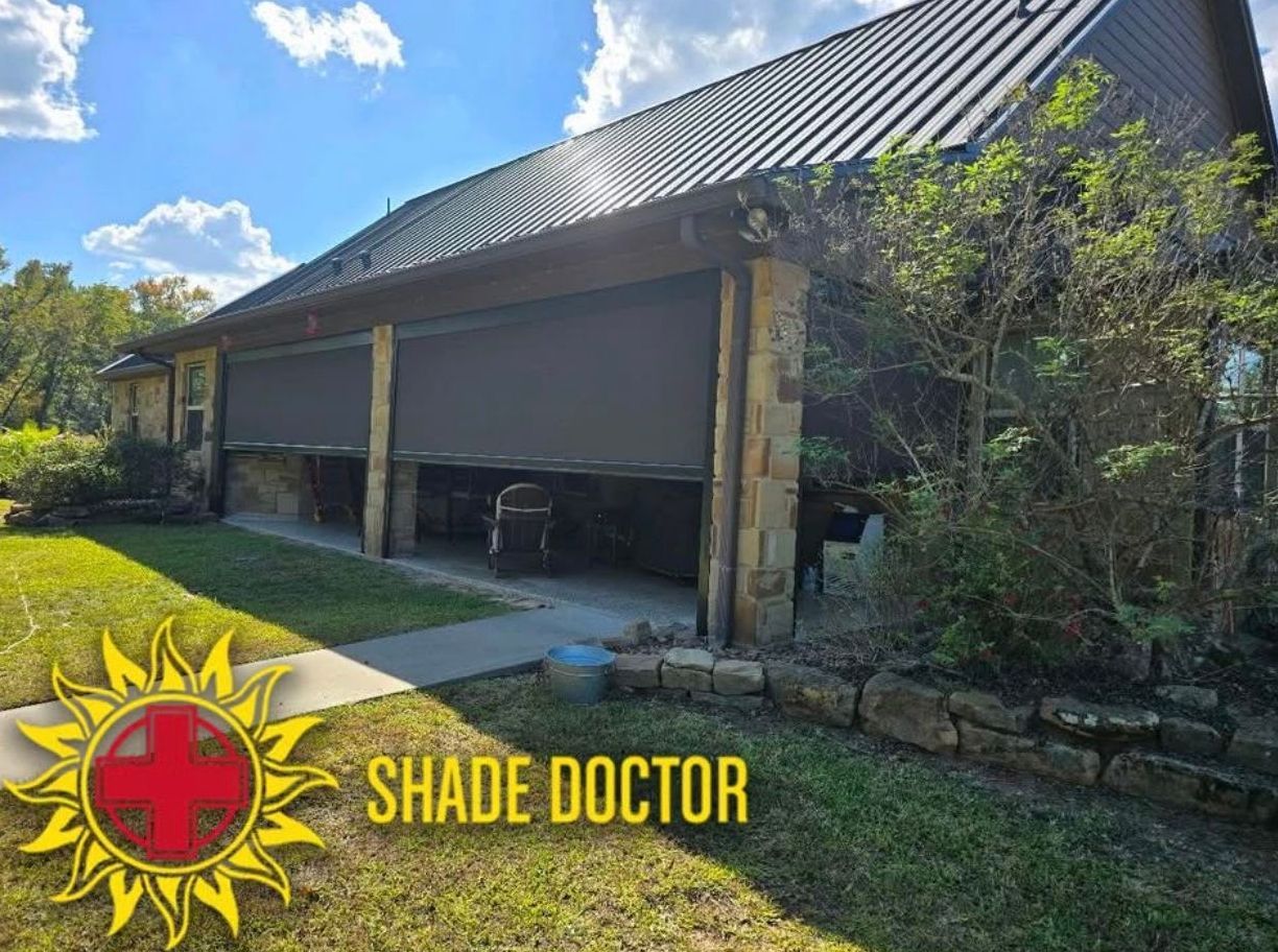 Large screened porch with dark metal roof and stone columns beside a green lawn under a blue sky.