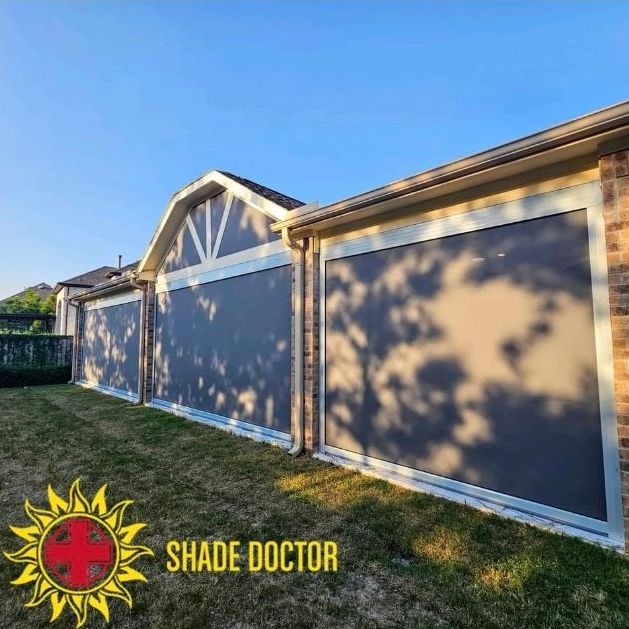 Blue house siding and a garage with large taupe shade panels in a sunny yard