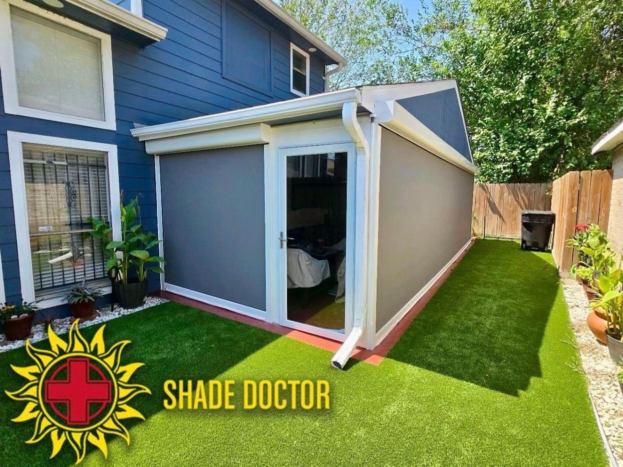 Gray outdoor shade shelter beside a house, with green artificial turf and fence in a sunny backyard