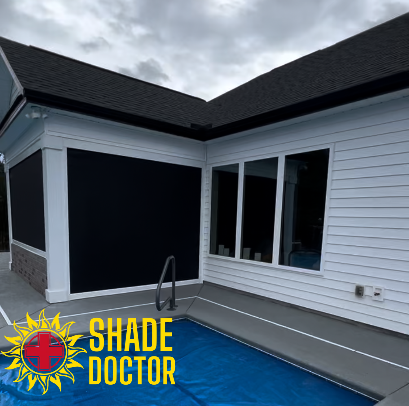 Patio with black retractable screen shades on a white house beside a pool