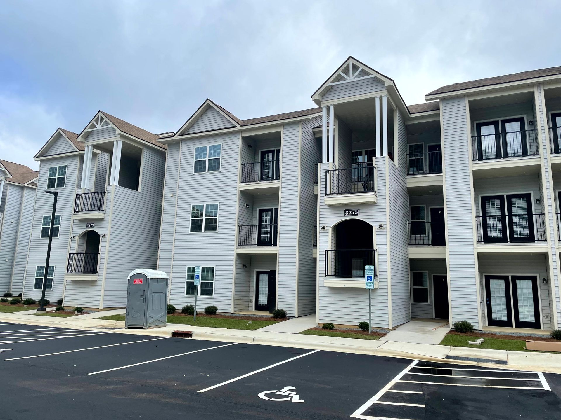Apartment complex exterior with gray siding, balconies, and parking spaces in front