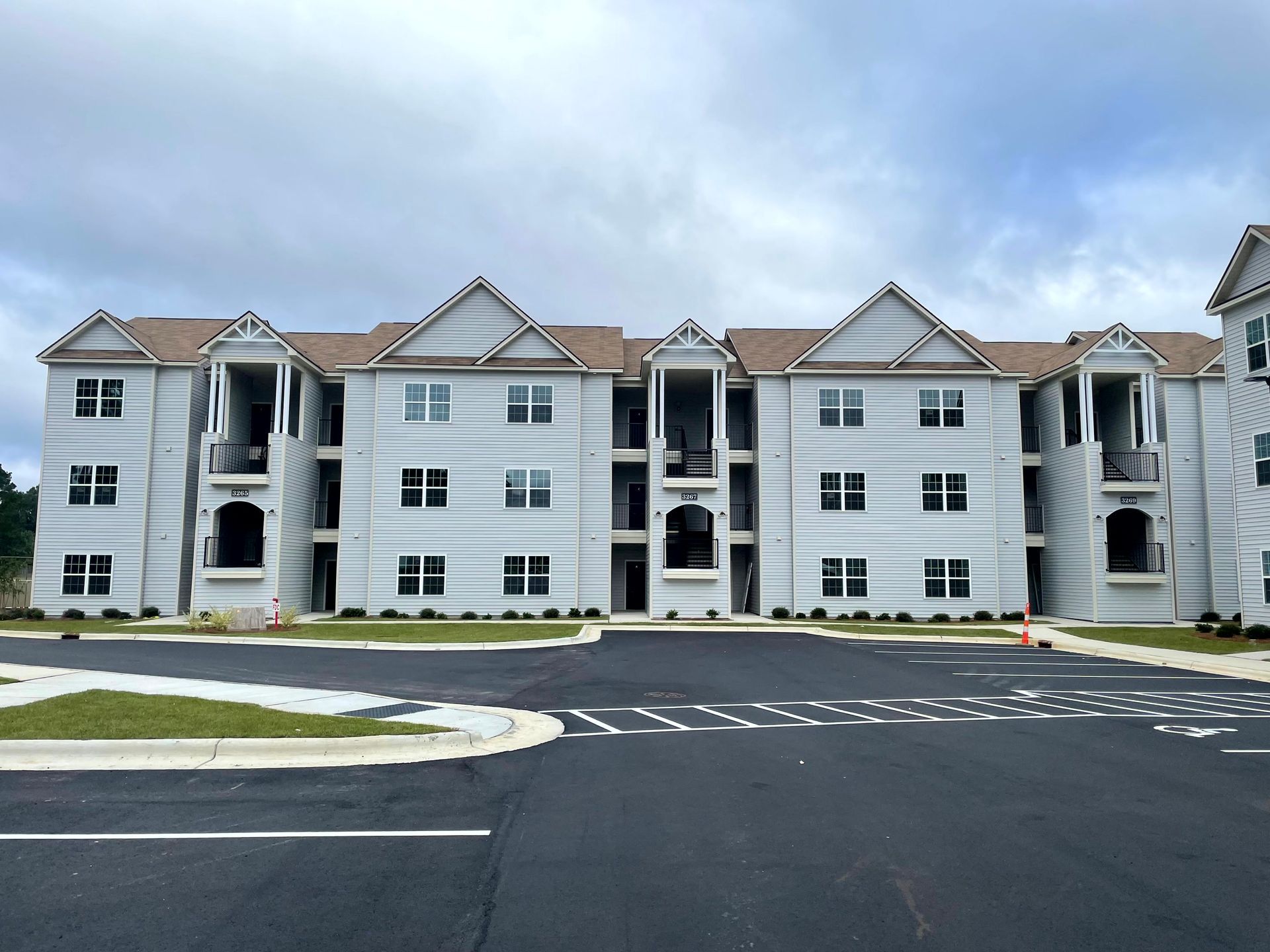 Apartment building exterior with white siding, gray roofs, and a dark driveway under a cloudy sky