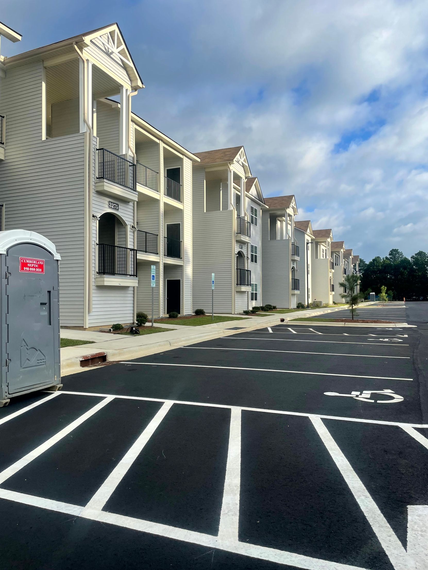 Apartment complex parking lot with white-striped spaces and a portable toilet on the left