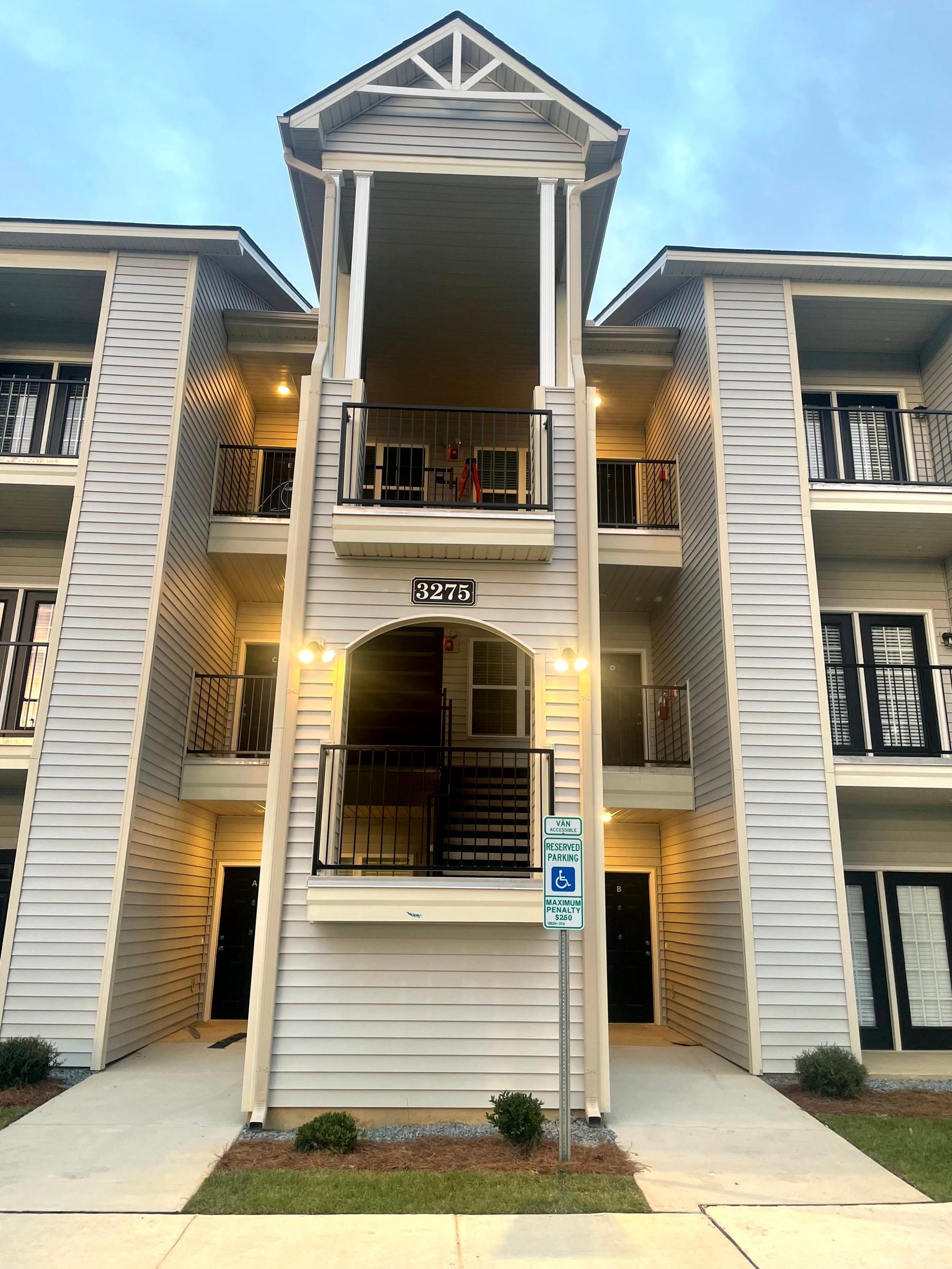 Apartment building entrance with central balconies, white siding, and lit stairwell openings