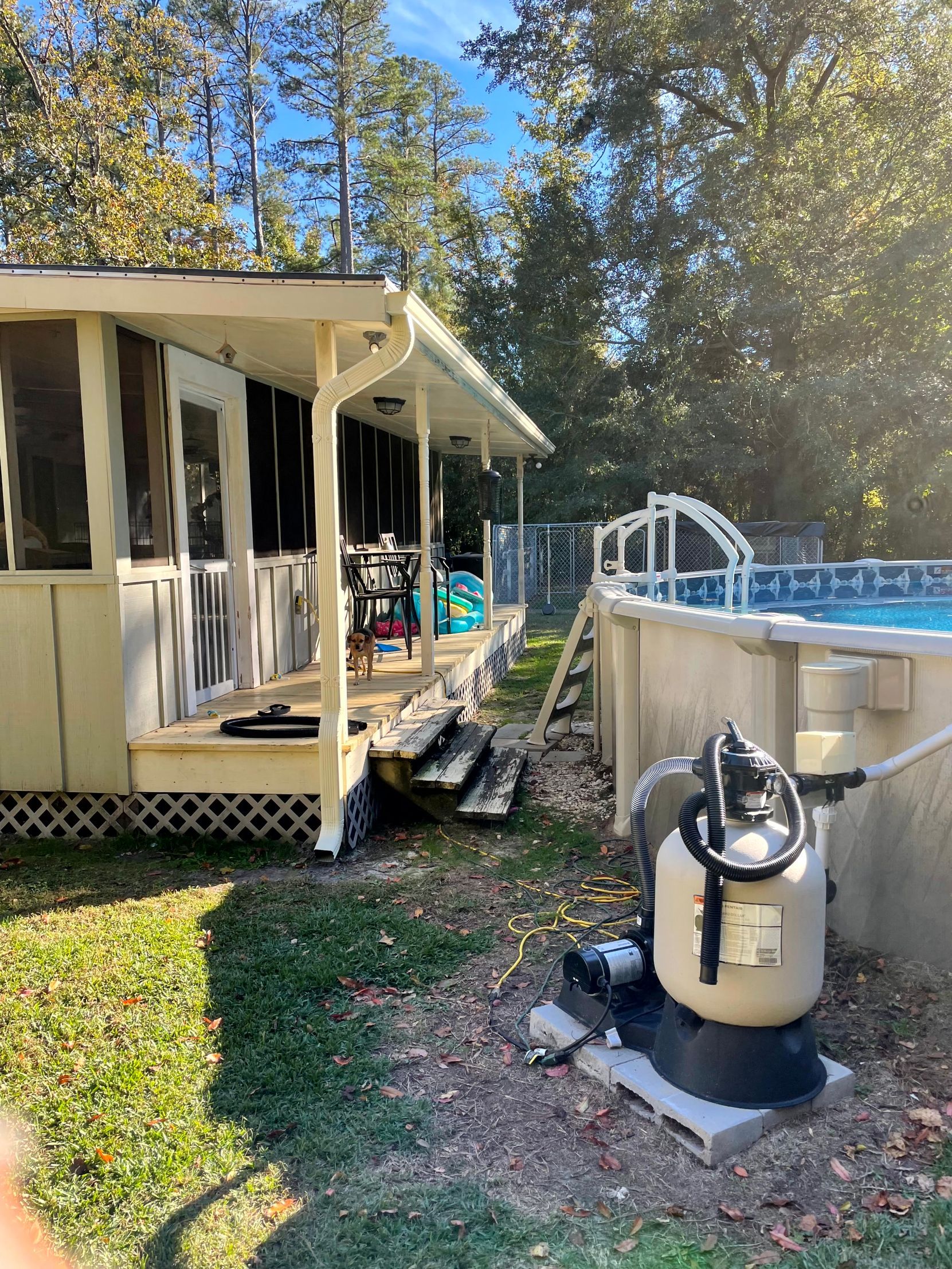 Backyard with screened porch beside an above-ground pool and a pressure washer on the grass
