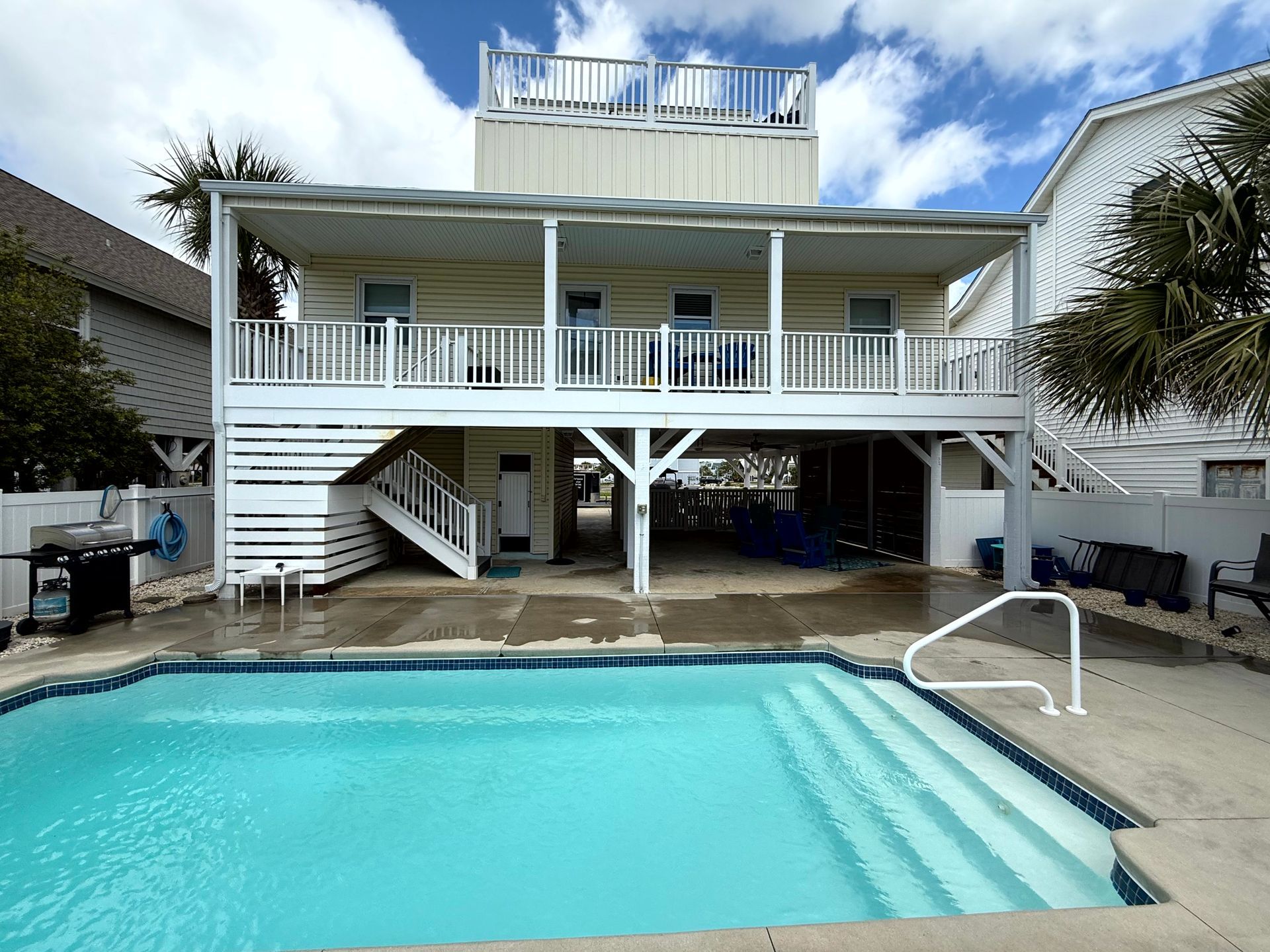 Backyard house with raised deck and turquoise swimming pool under a partly cloudy sky