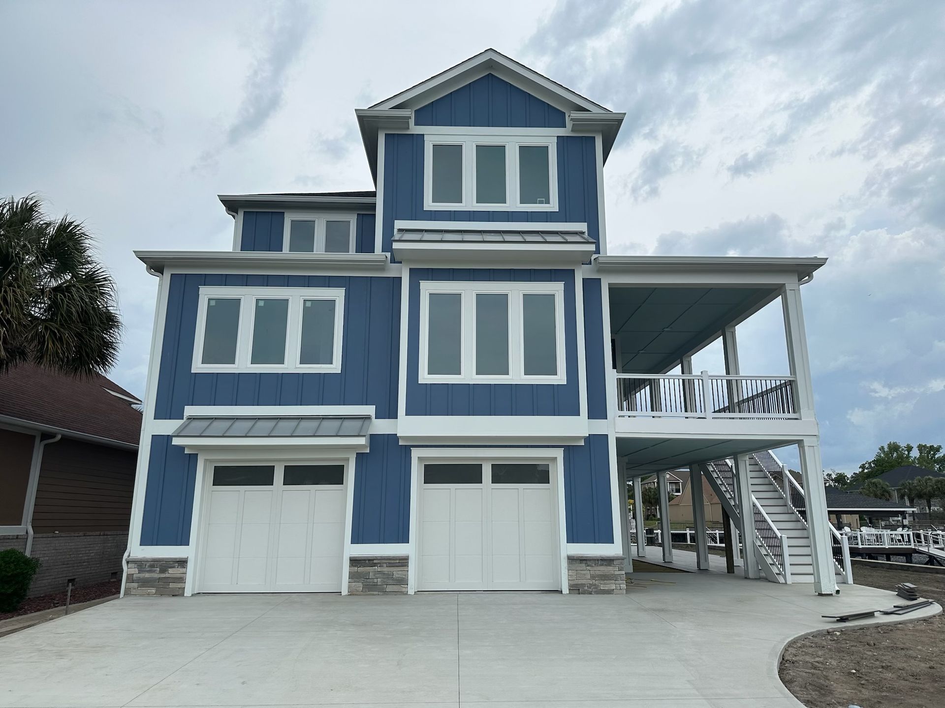 Blue three-story house with white trim, two garage doors, and an elevated porch under construction