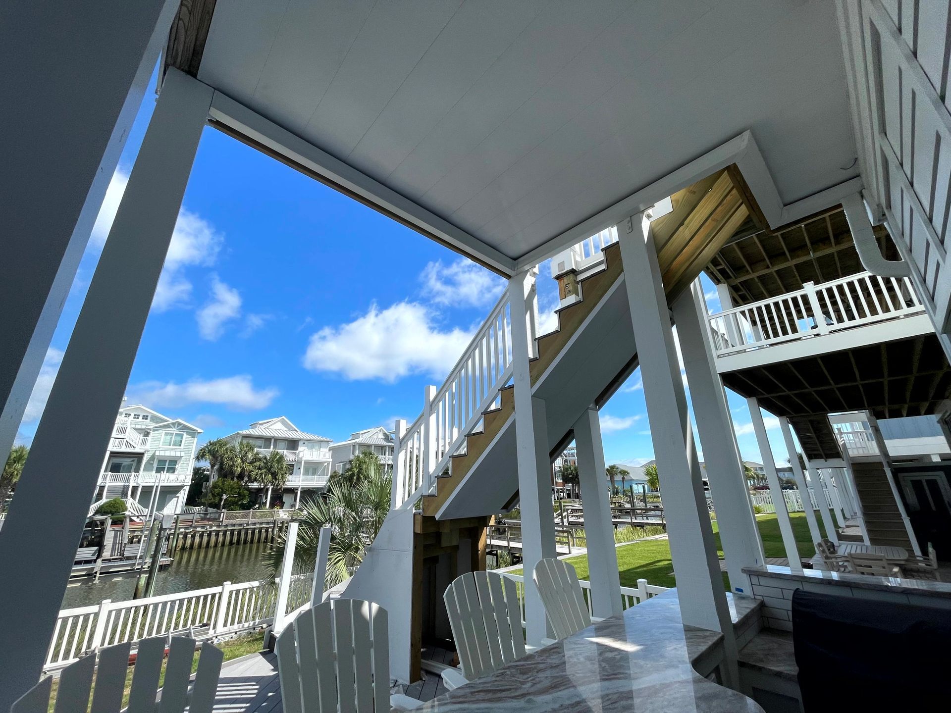 Porch with white railings and stairs overlooking a sunny waterfront neighborhood under a blue sky