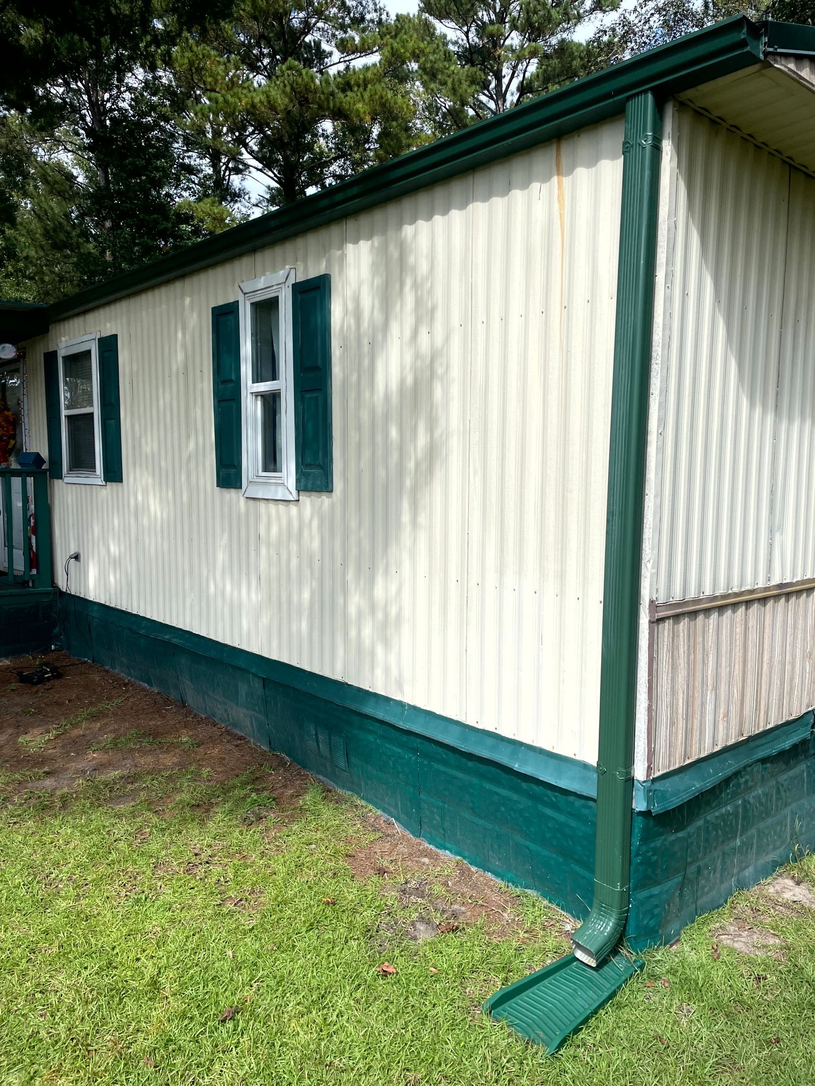 Cream and green mobile home with windows, shown beside a grassy yard and trees.