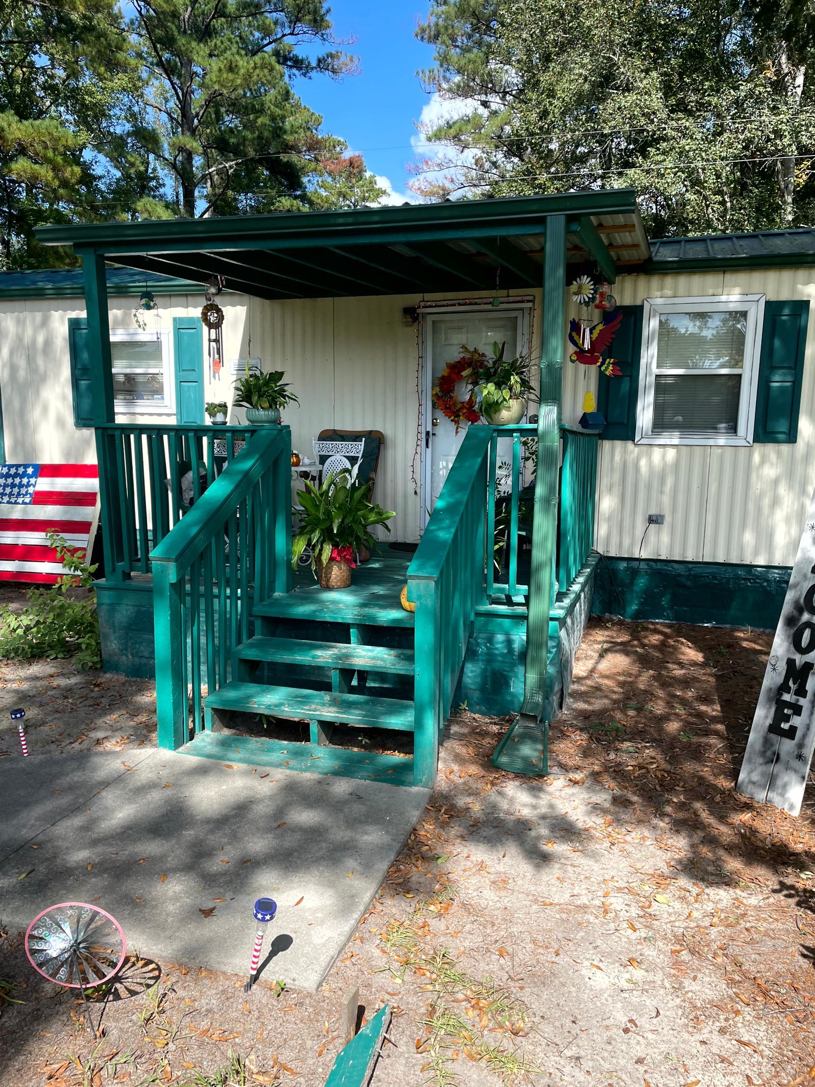 Teal porch steps lead to a small white house with green shutters and an American flag on the left.