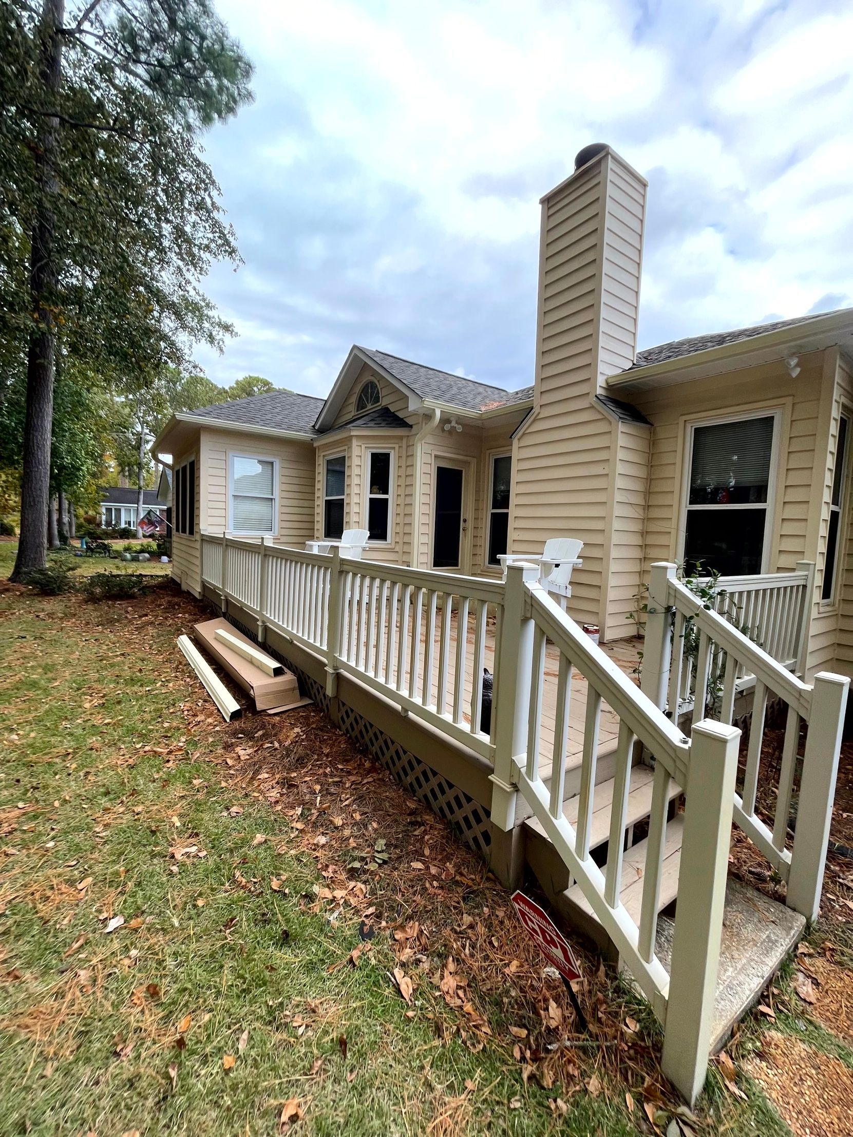 Small beige house with a white porch railing, tall chimney, and fallen leaves in the yard.