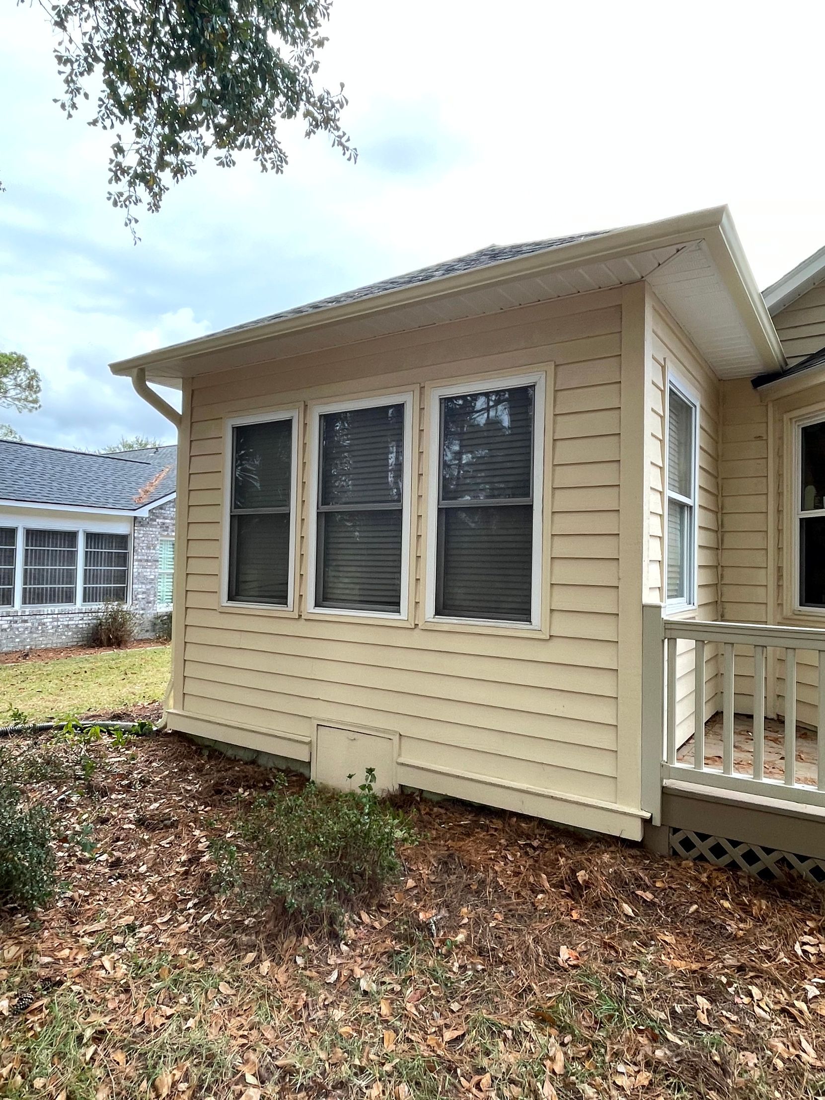 Beige house exterior with three windows, white trim, and a small porch surrounded by fallen leaves