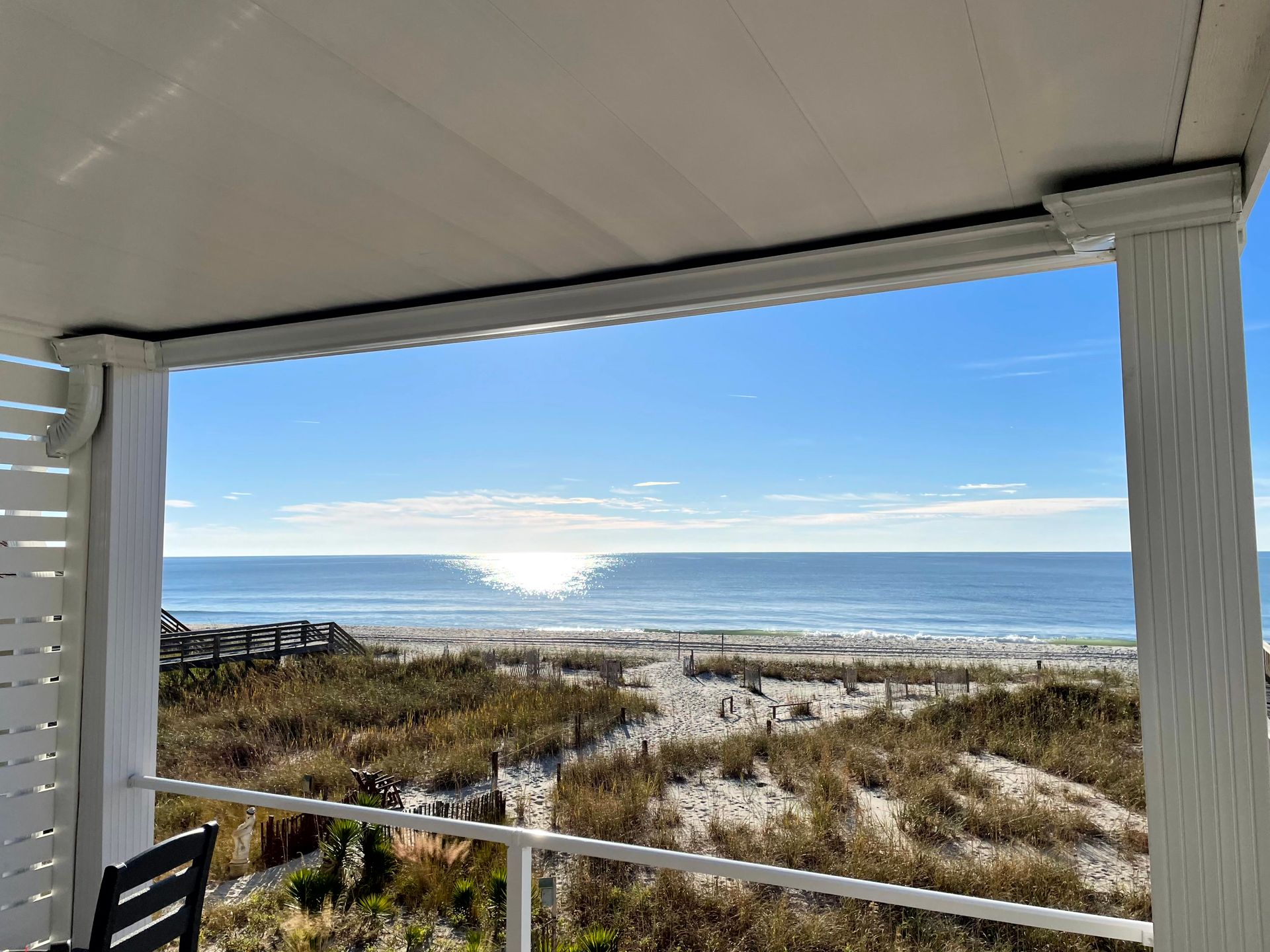 Covered porch overlooking sandy beach and calm ocean under a blue sky