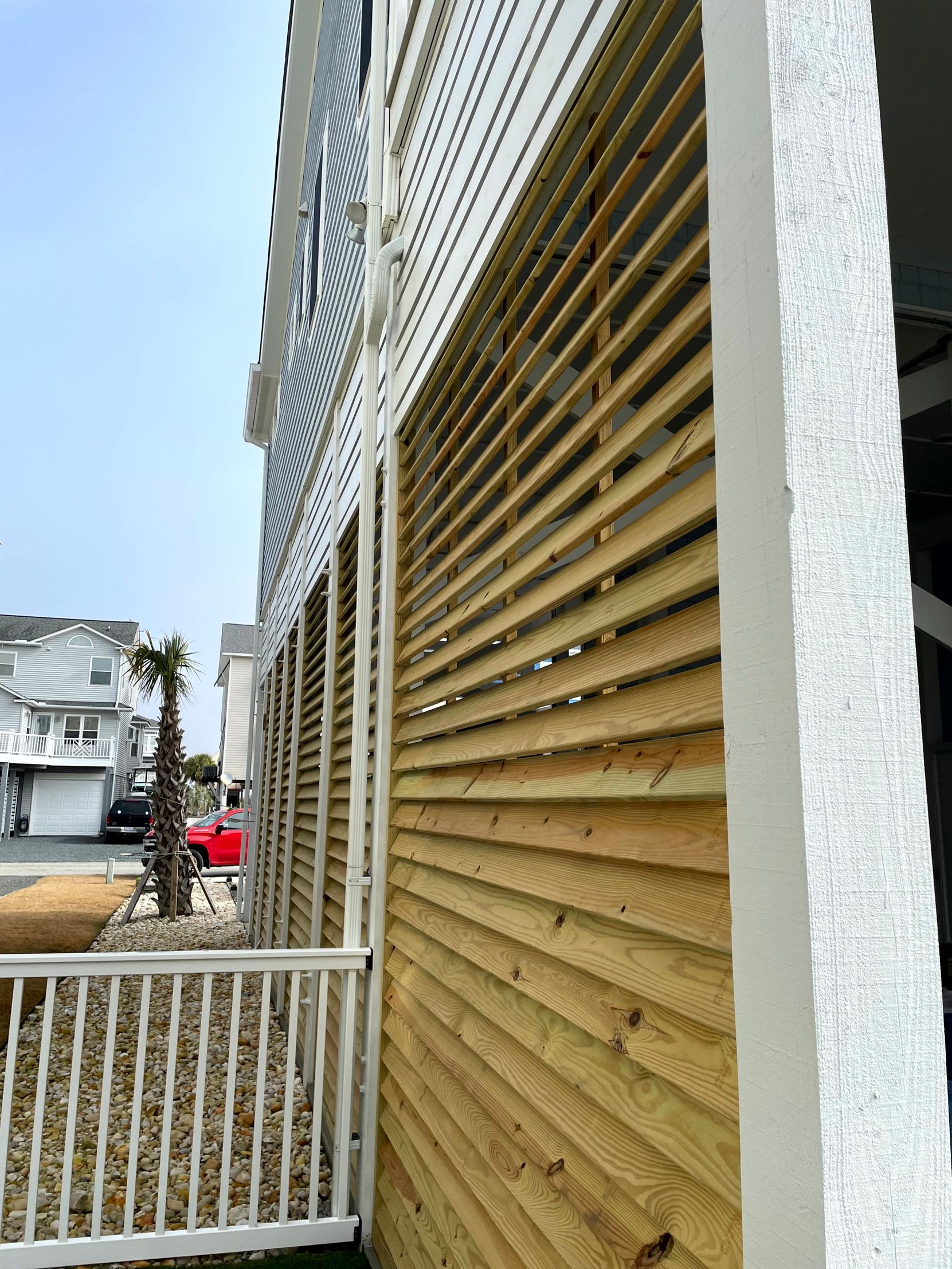 Exterior of a house with white trim and tan slatted shutters, viewed from a side walkway.
