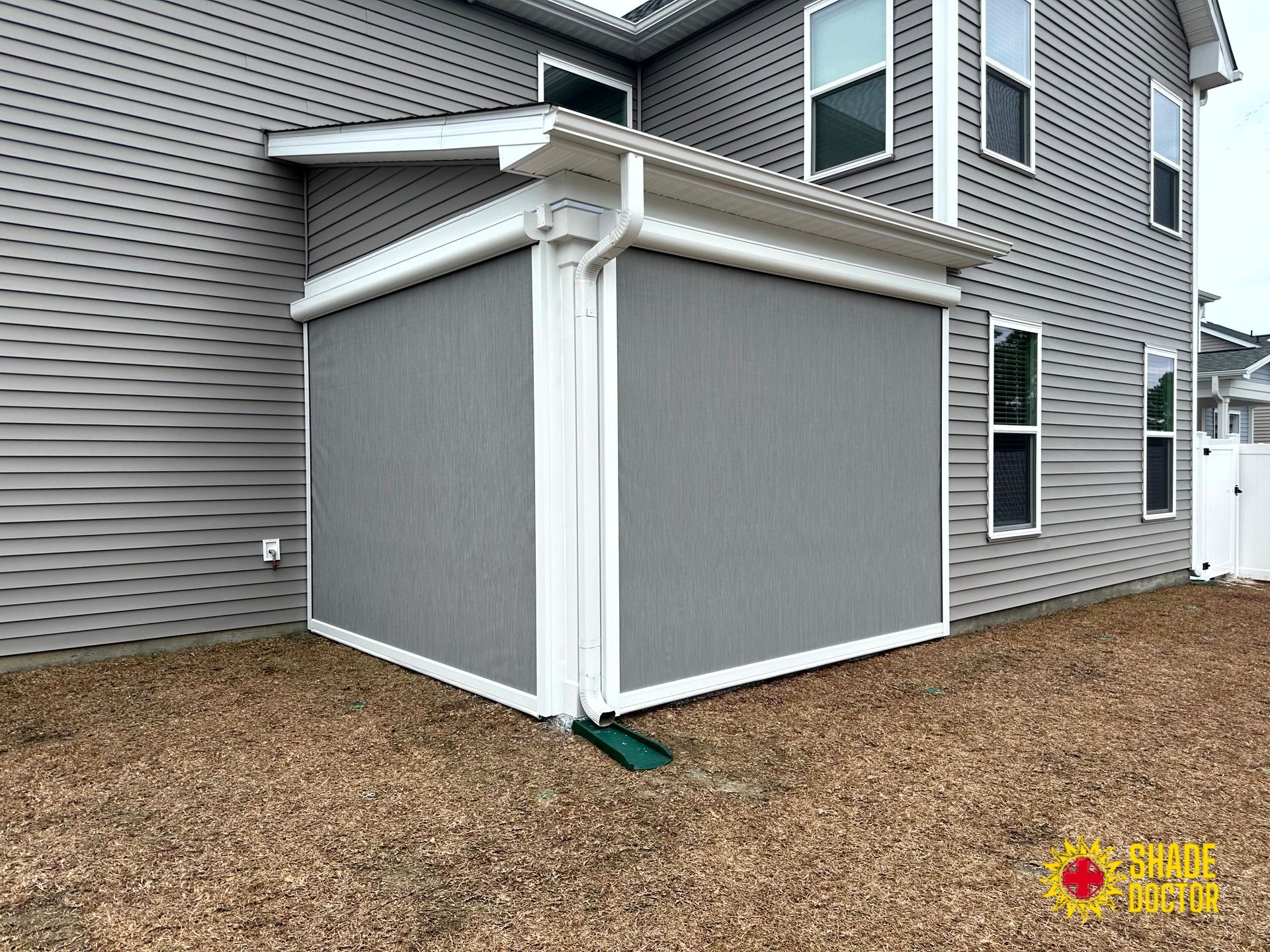 Gray-sided house with a white screened porch enclosure under a covered deck, beside a mulch yard.