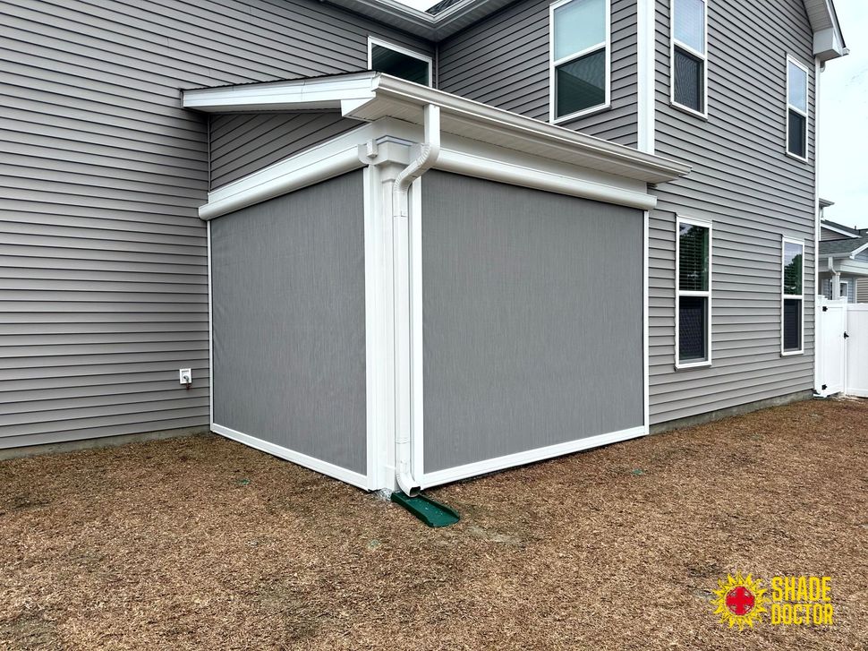 Gray vinyl-sided house with a white enclosed patio structure in a mulched backyard