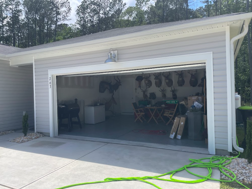 Open garage with patio furniture and storage inside, green hose on concrete driveway.