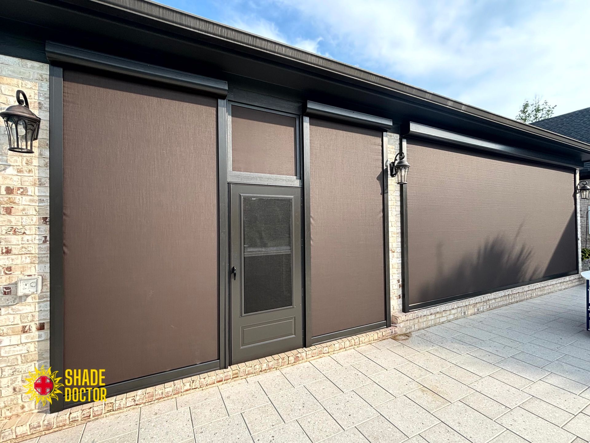 Brown exterior roller shutters and a door on a building facade beside a paved driveway