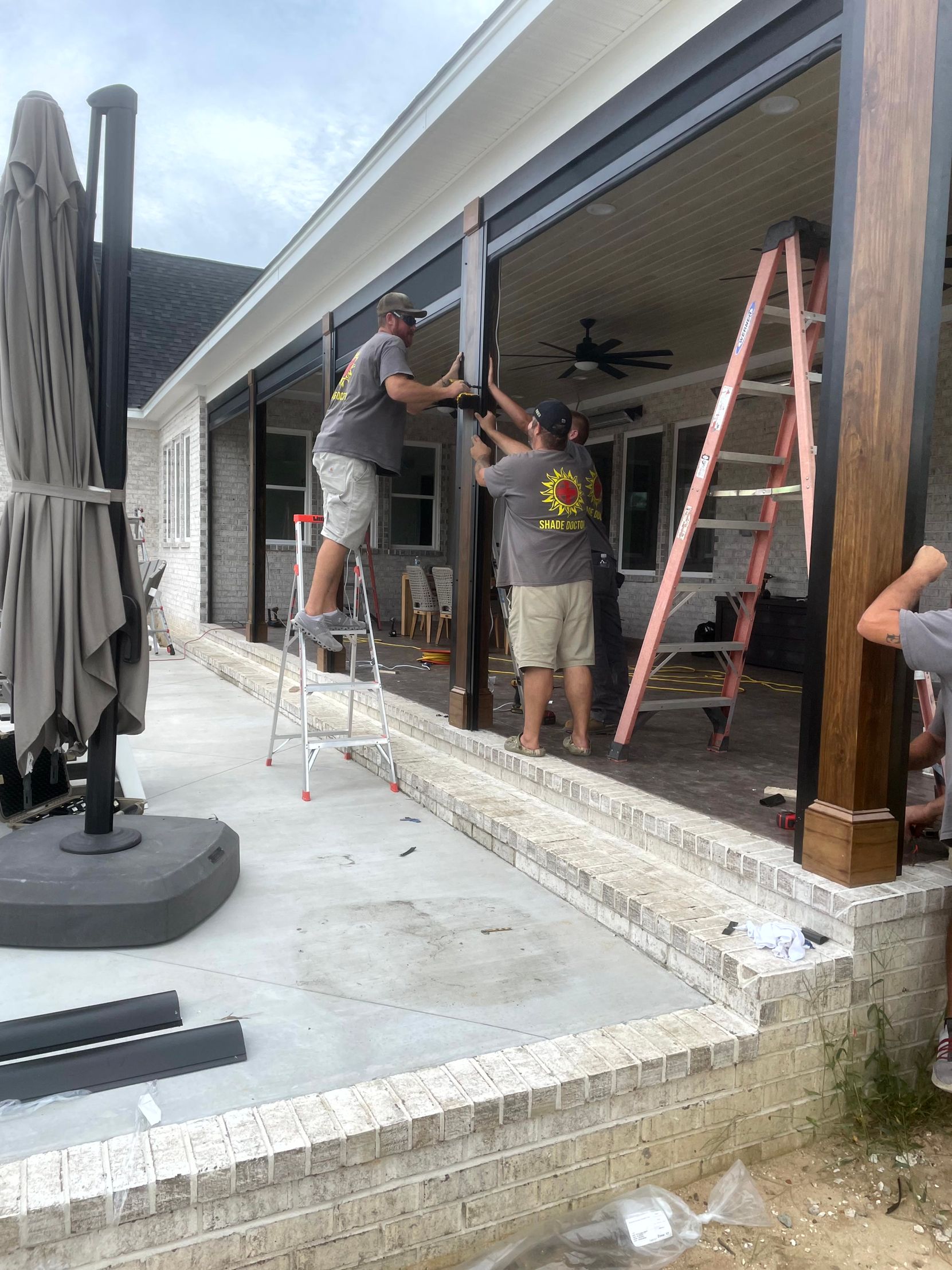 Workers installing a large glass garage door on a house under construction, with ladders and tools nearby