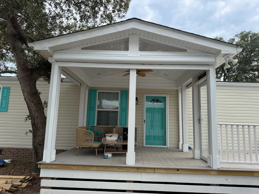 Front porch with teal door, white columns, and bench under a gabled roof