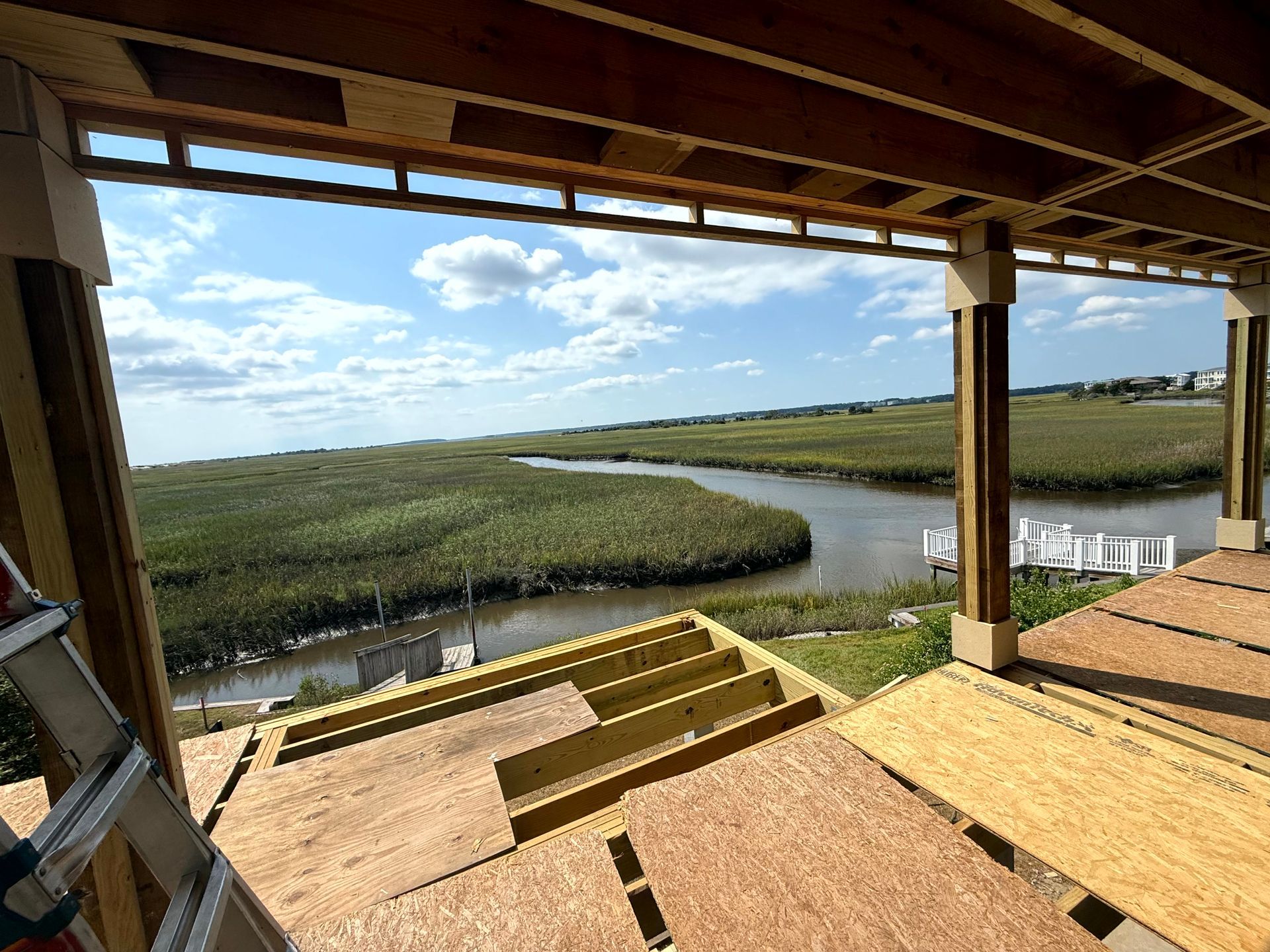 Covered wooden deck overlooking a marsh and winding waterway under a partly cloudy sky.