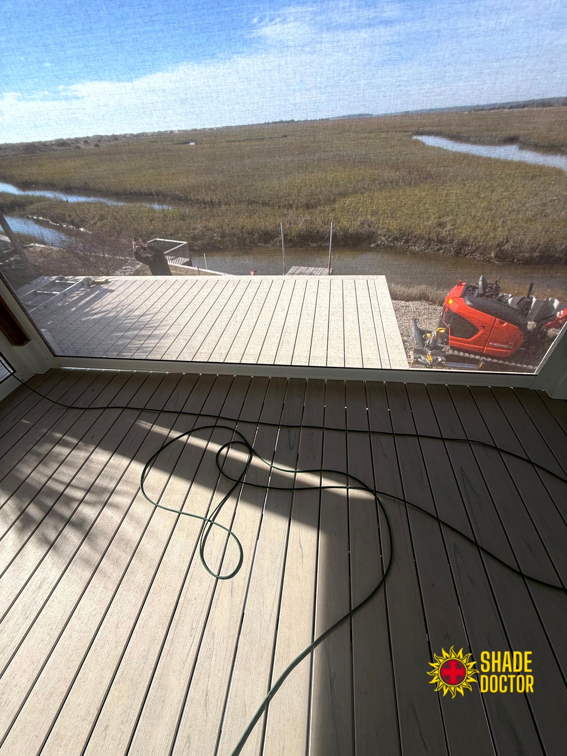 Flooded field viewed from a deck, with a red boat at right and cables on the floor in the foreground