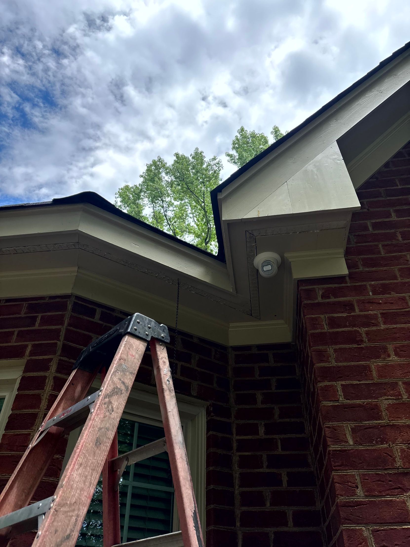 Brick house exterior with ladder under the eaves and cloudy sky above