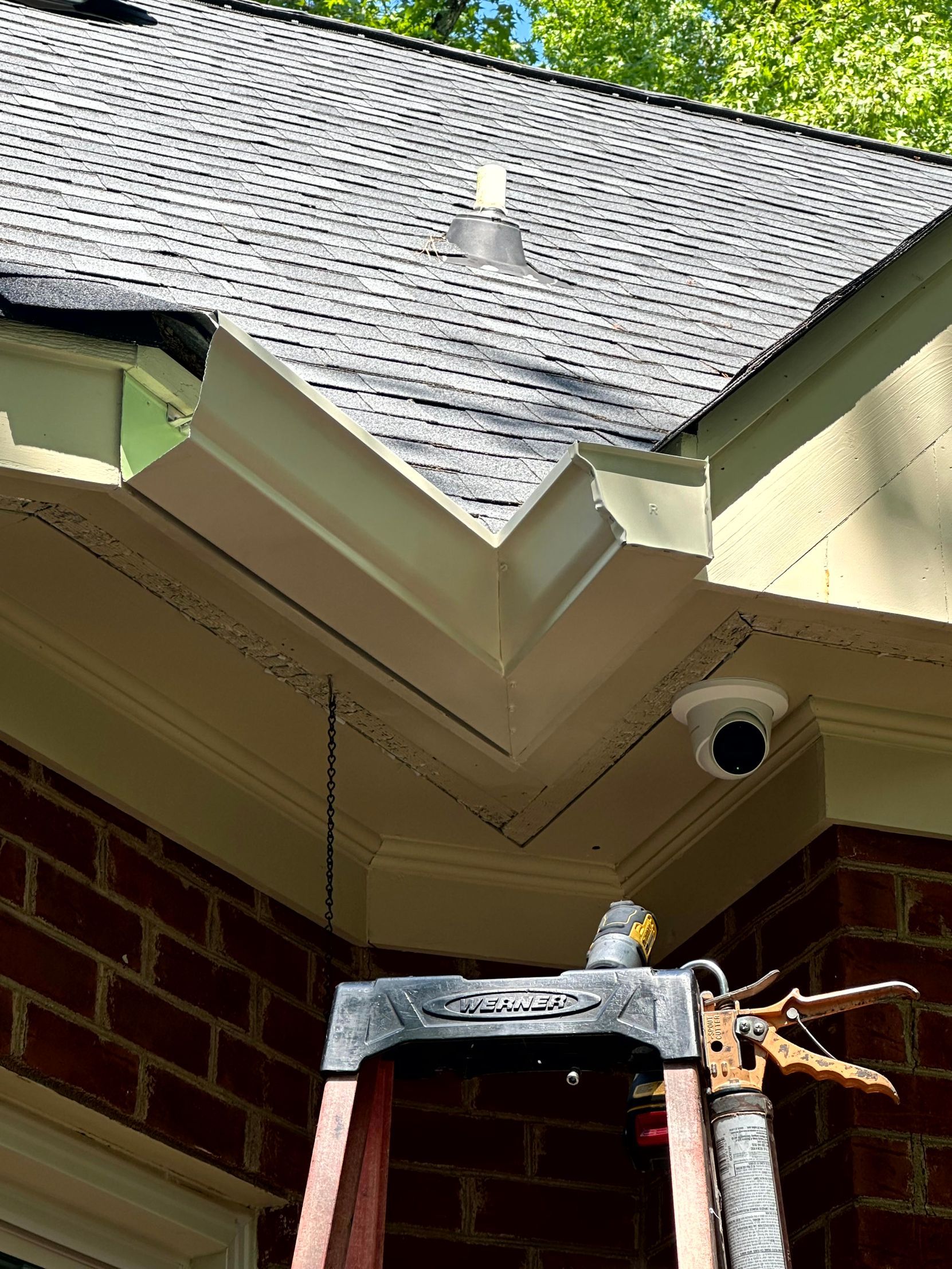 House eaves with a steep roof, gutter corner, and a ladder beneath an overcast sky