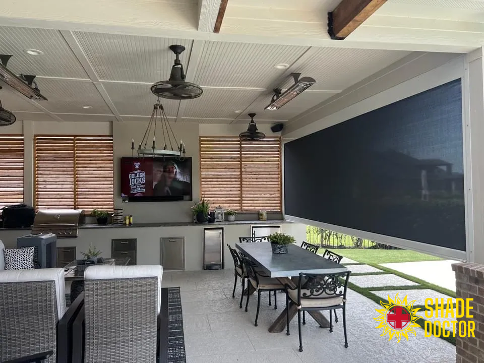Covered patio with seating, ceiling fans, TV, and outdoor dining table beside a lawn.