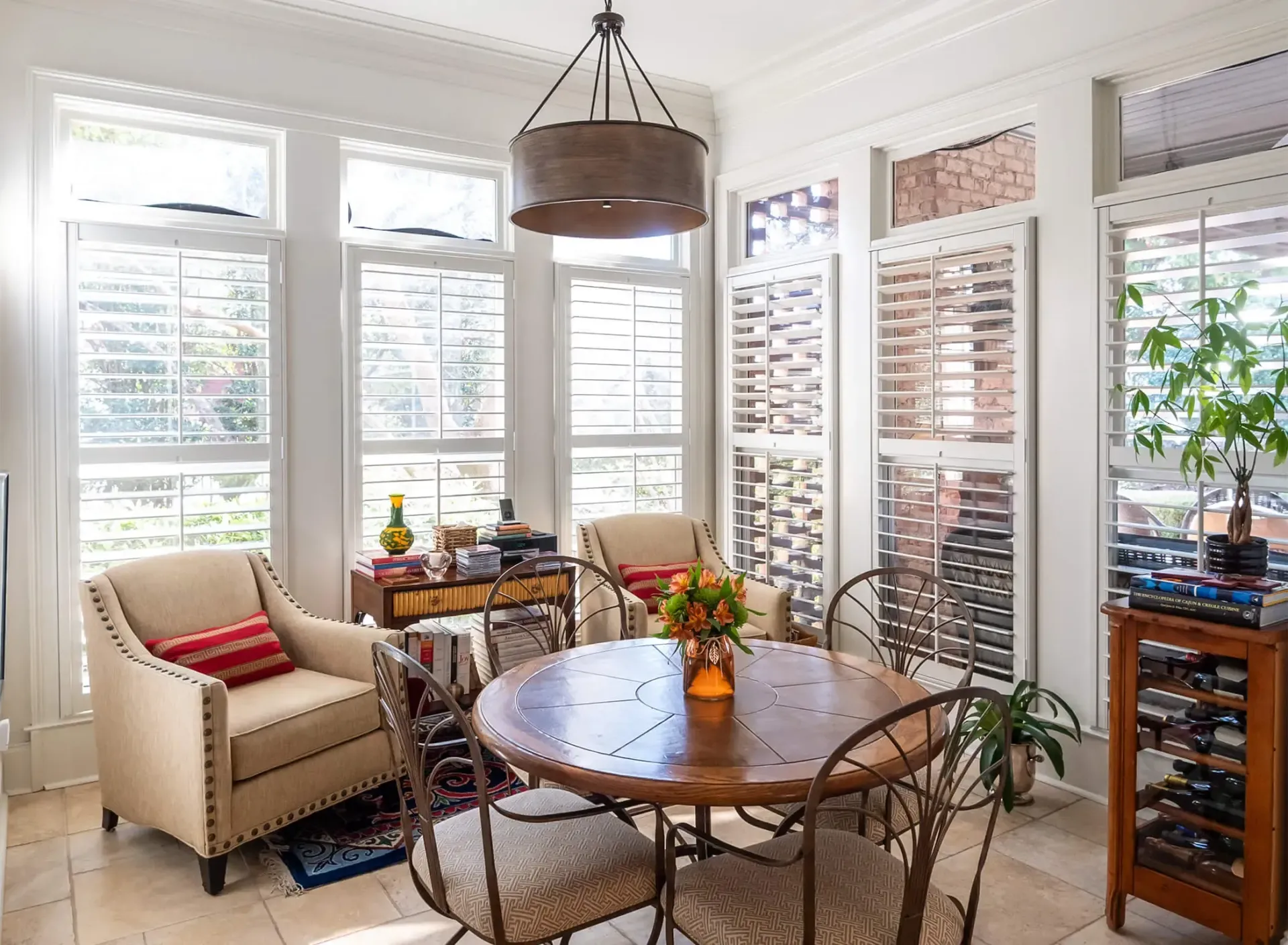 Bright sunroom with wicker table, beige chairs, plants, and large windows with blinds
