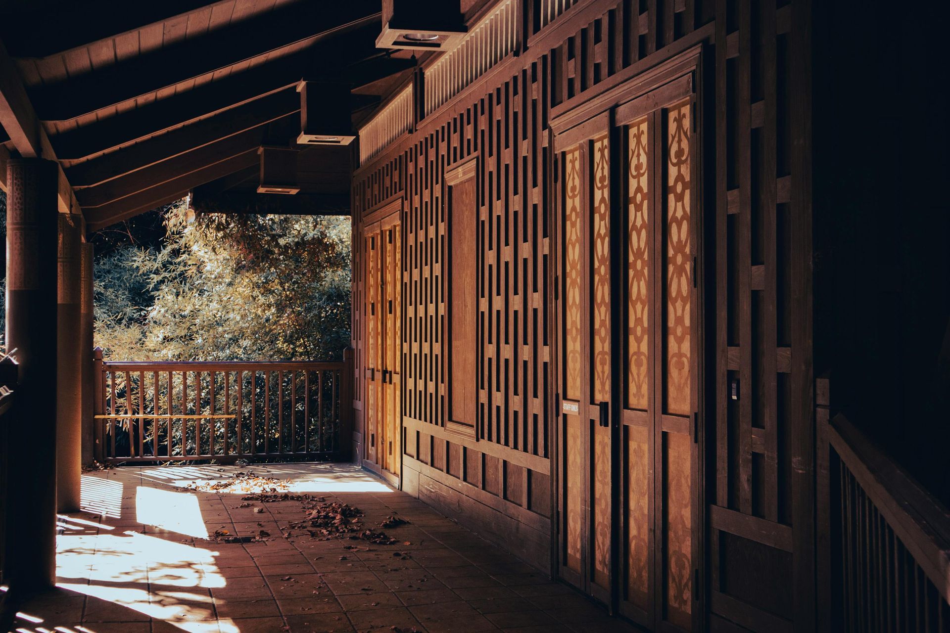 Wooden porch corridor with sunlight, railings, and trees beyond