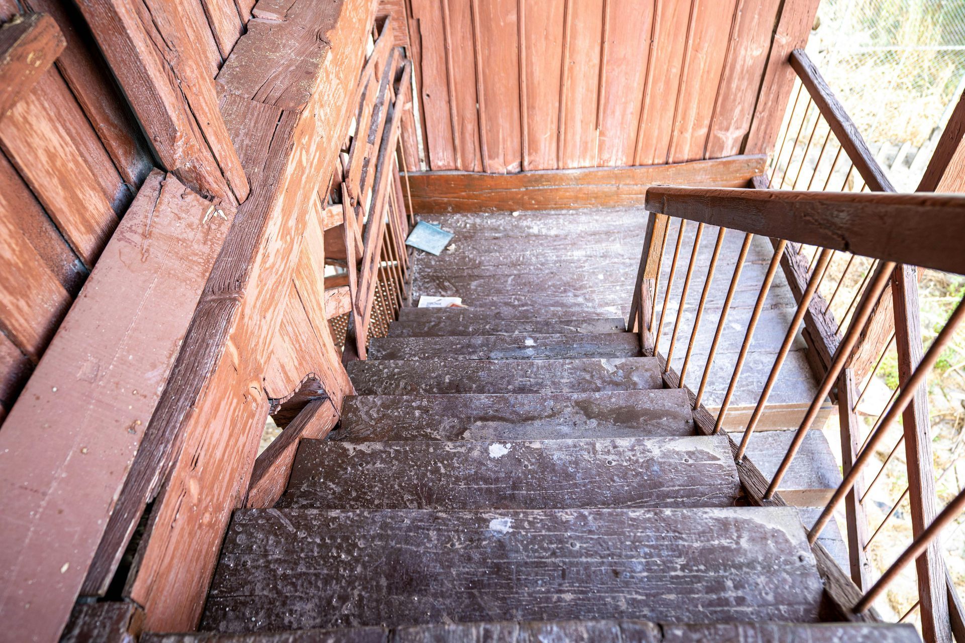 Weathered wooden stairway descending beside a log wall and metal railing