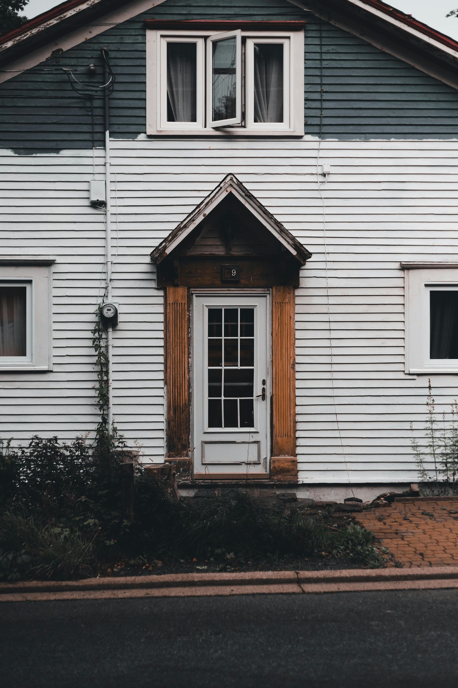 White house exterior with dark green upper siding, front door, and small peaked awning above the entrance