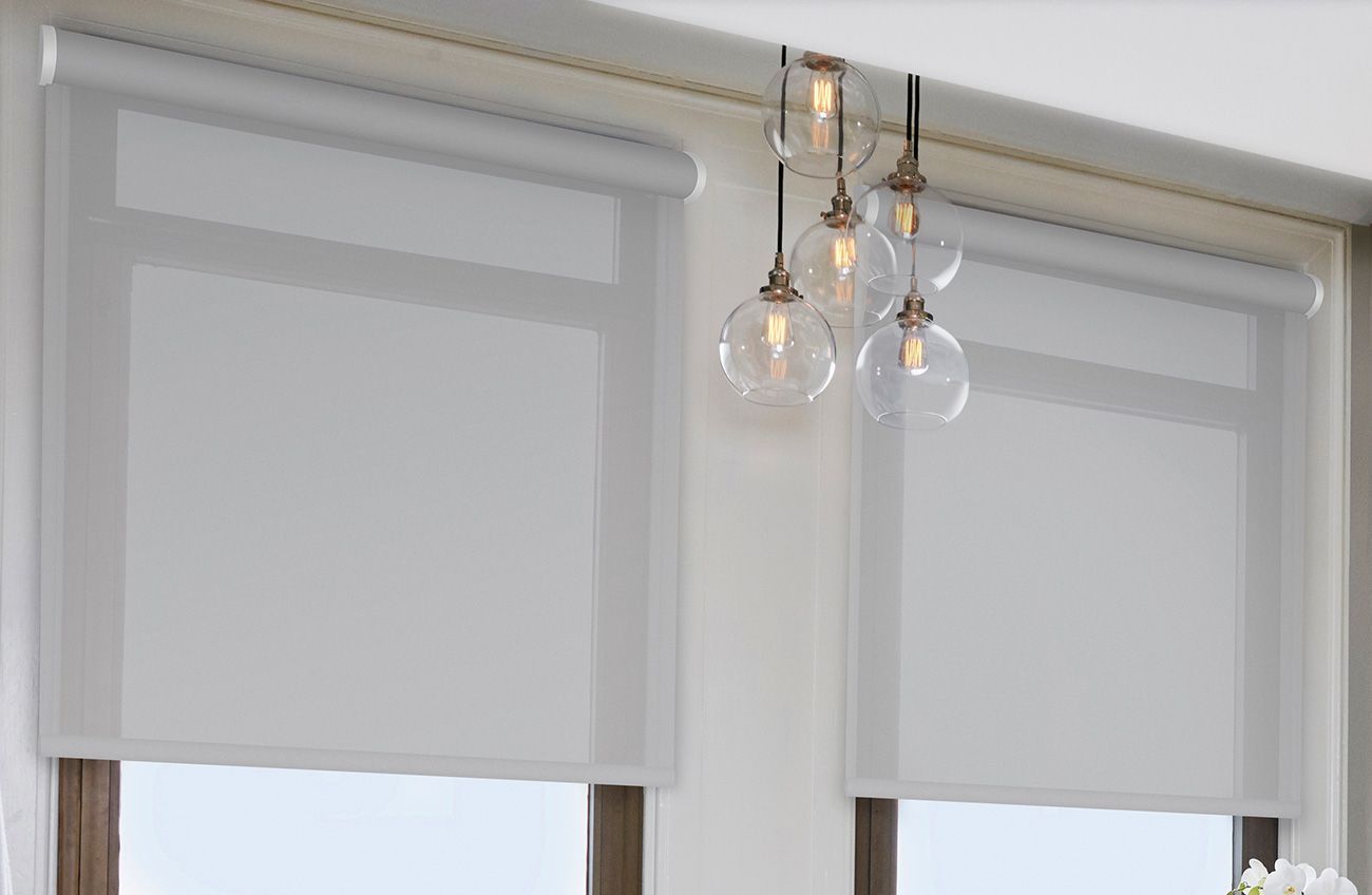 White roller shades over two windows with a gold pendant light in the center.
