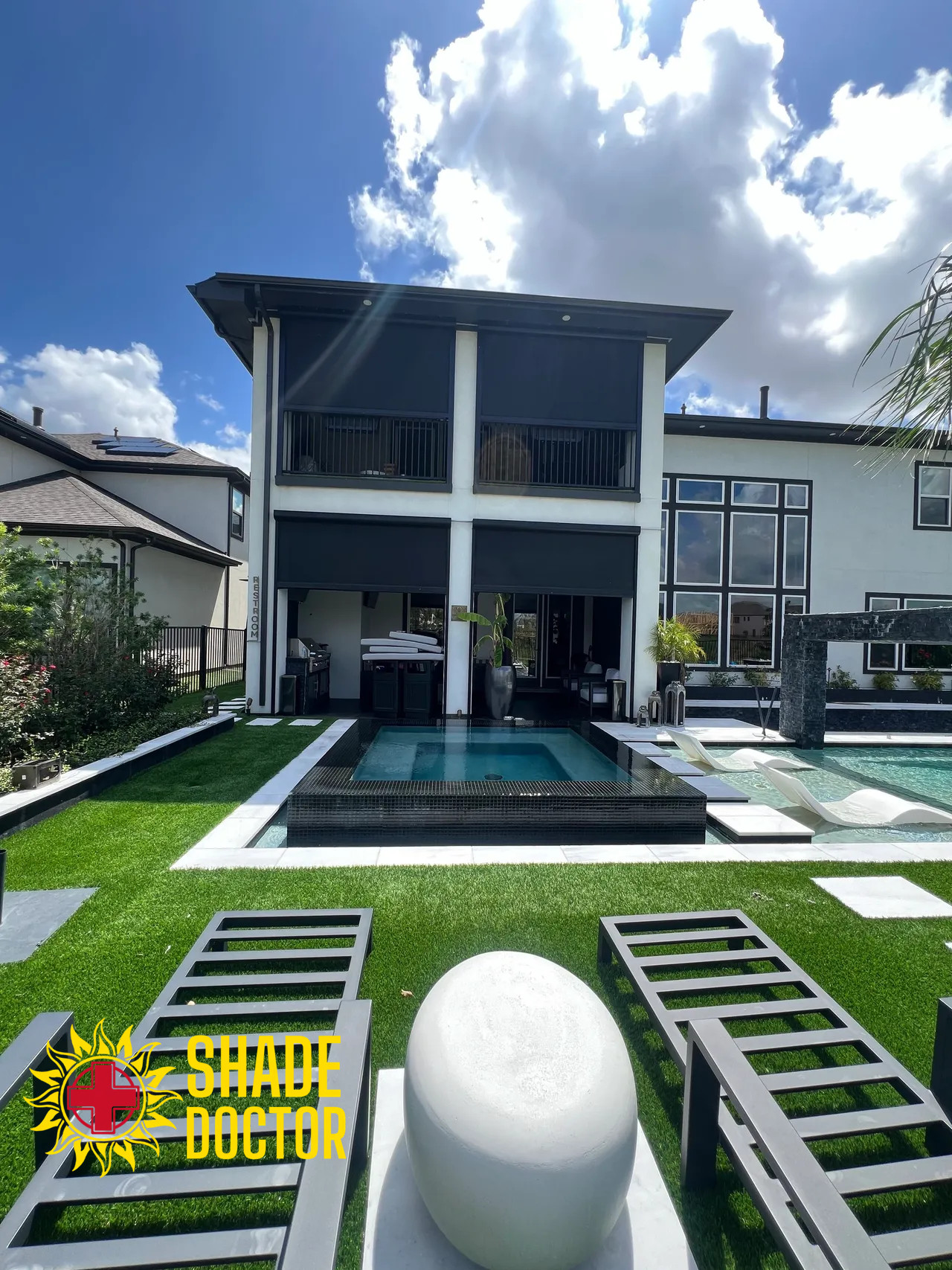 Modern two-story house with pool, green lawn, and lounge chairs under a partly cloudy sky