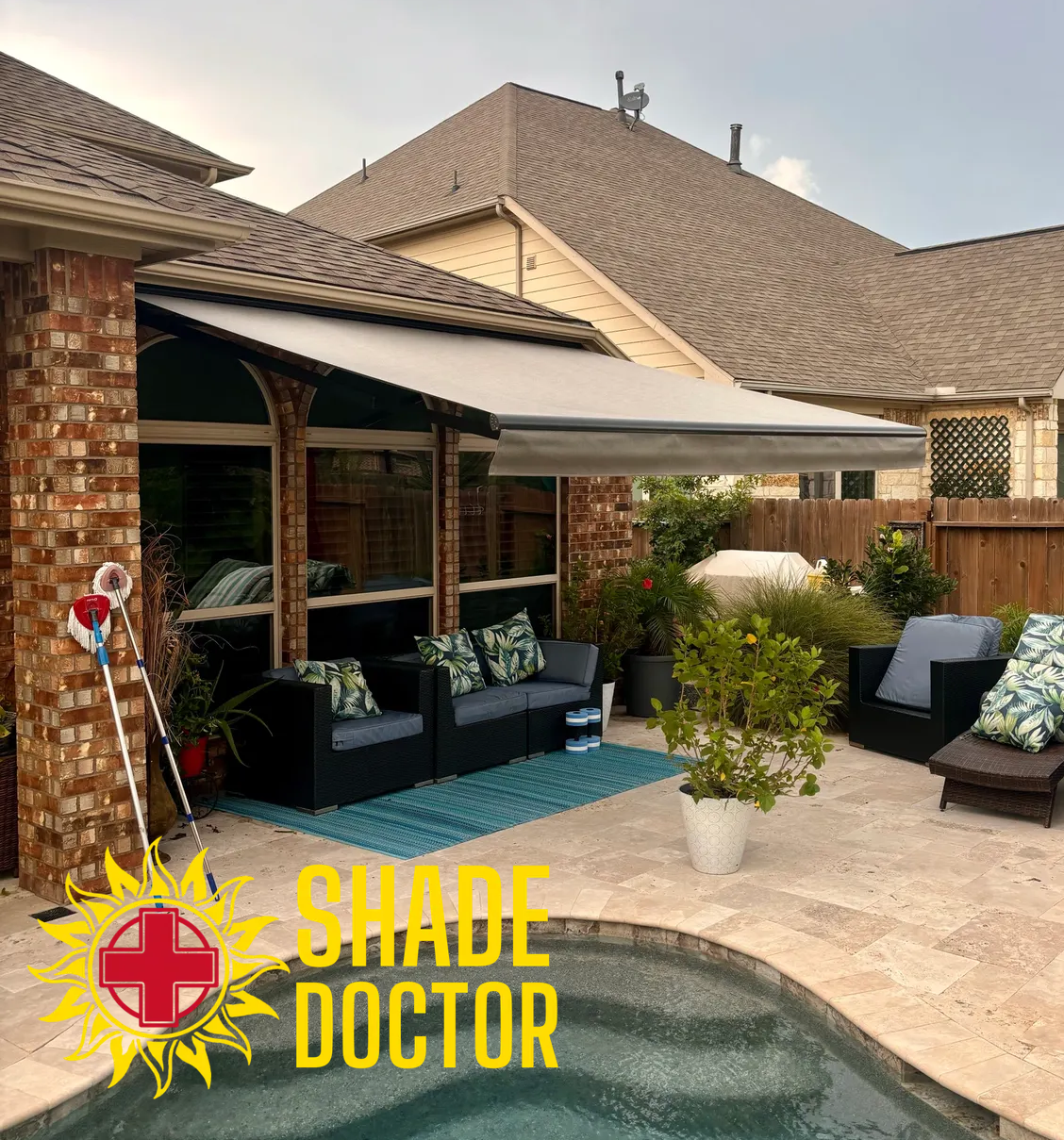 Patio with shade sail over seating area beside a swimming pool, with Shade Doctor logo.