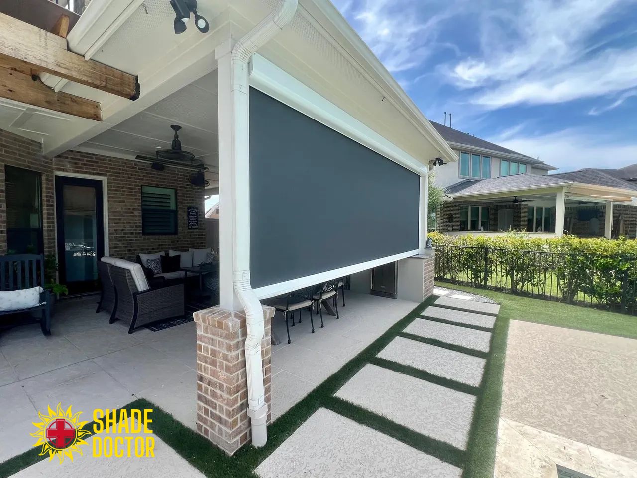 Backyard patio with gray retractable screen, stone columns, outdoor seating, and stepping stones along the lawn