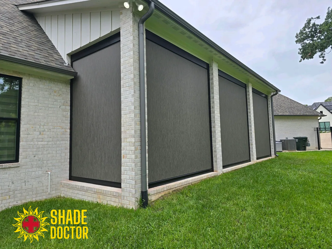 House exterior with large gray outdoor privacy screens over patio openings and a green lawn.