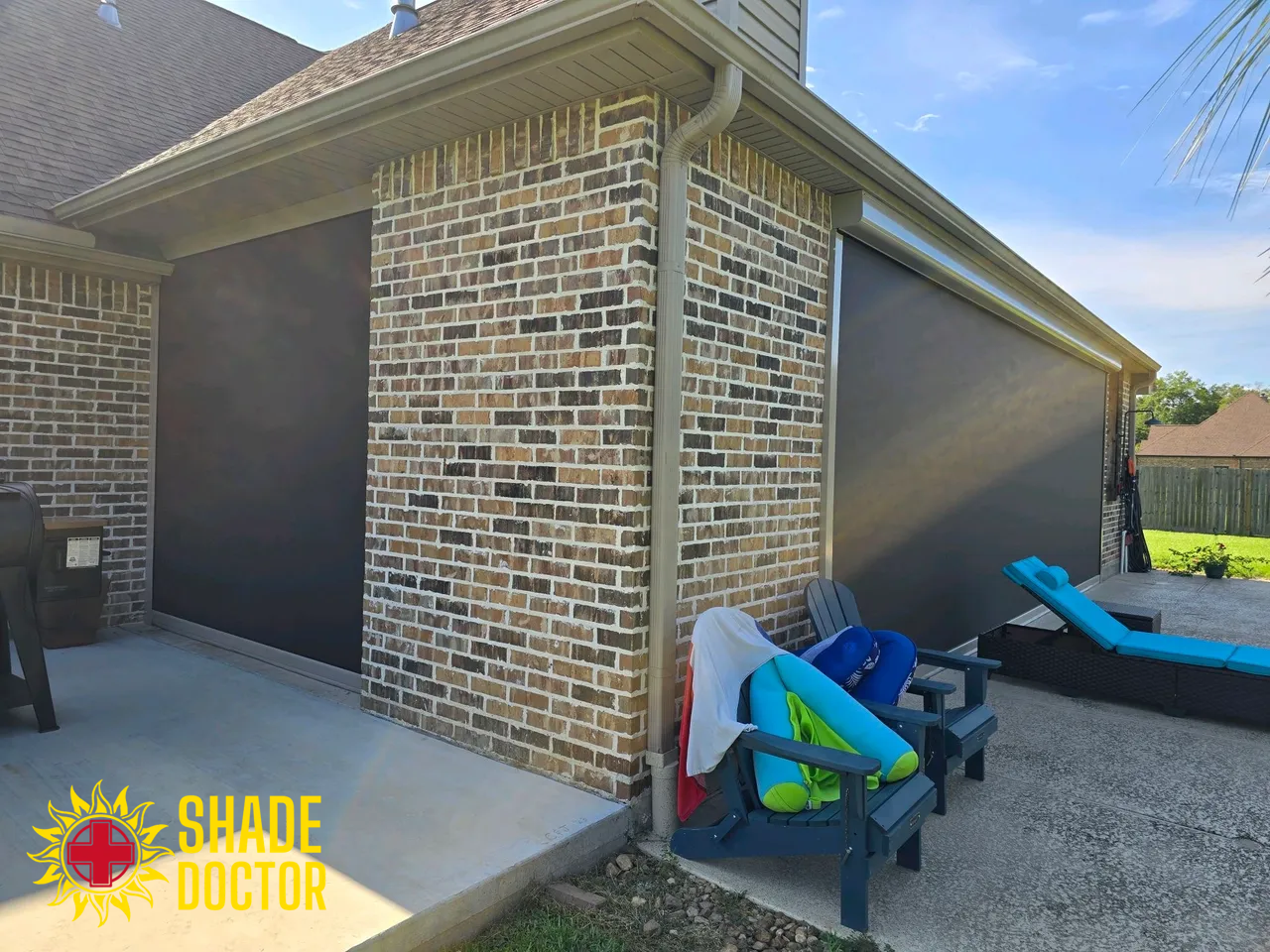 Brick house corner patio with outdoor chairs, blue lounge seat, and gravel ground under a clear sky