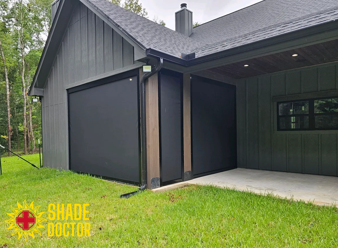 Dark gray house exterior with large black garage doors and a covered patio on a green lawn