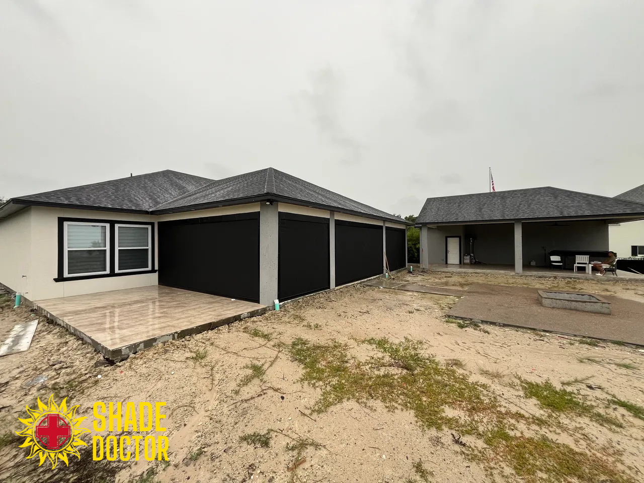 Two newly built single-story homes with dark roofs and unfinished dirt yard under an overcast sky