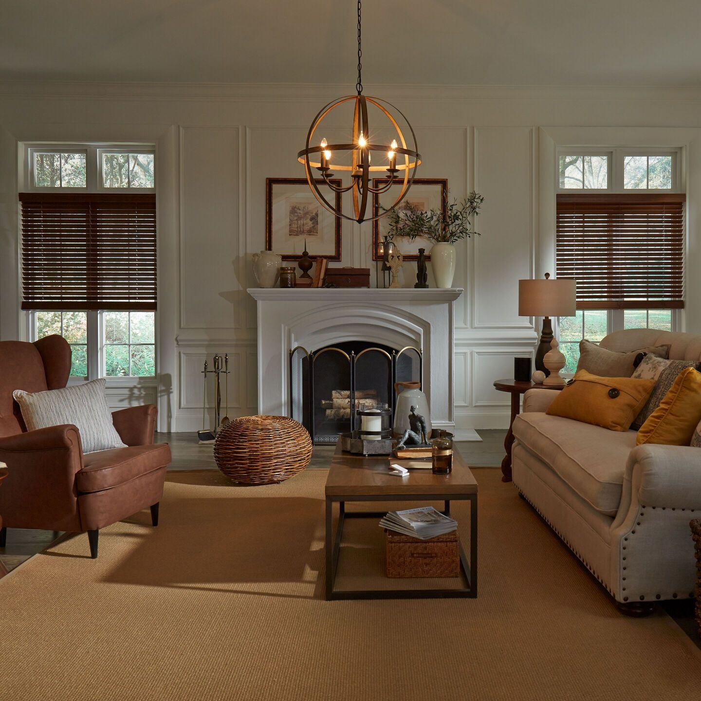Cozy living room with fireplace, beige sofa, armchairs, coffee table, and warm window blinds
