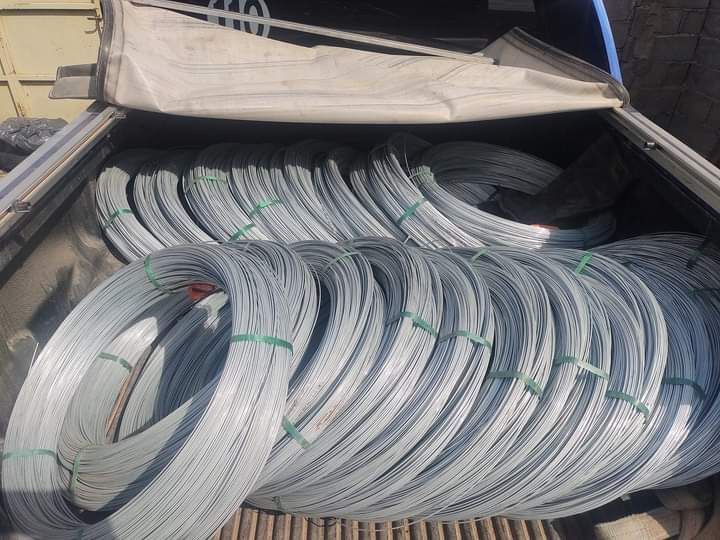 Bobinas de alambre de plata atadas con bridas verdes, llenando la parte trasera de un camión debajo de una lona blanca.