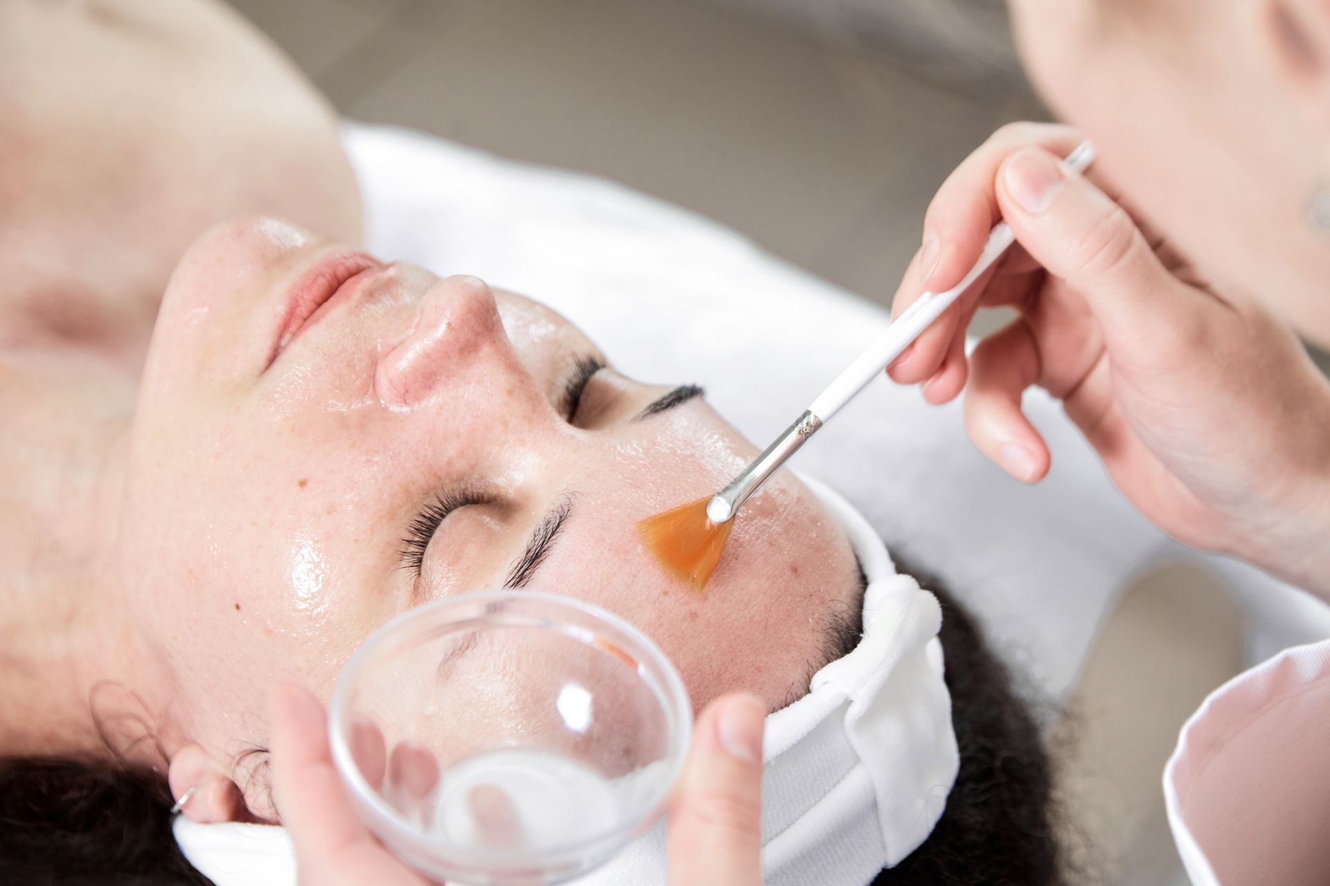 Facial spa treatment with a brush applying orange serum to a woman's face