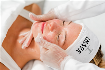 Facial spa treatment with gloved hands massaging a client’s face, eyes closed and covered by a white headband