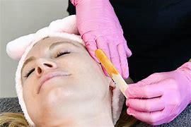 Woman getting facial waxing by gloved hands; pink gloves and headband.